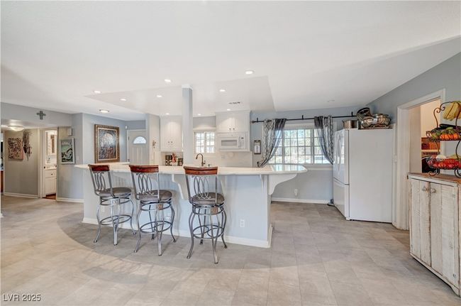 Kitchen featuring white appliances, a breakfast bar area, white cabinets, light countertops, and a sink | Image 57