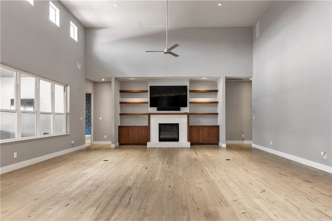 Unfurnished living room featuring a high ceiling, ceiling fan, light wood-style flooring, and a glass covered fireplace | Image 5