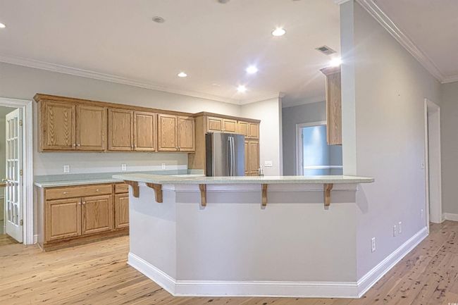 Kitchen featuring freestanding refrigerator, crown molding, a kitchen breakfast bar, light countertops, and light wood finished floors | Image 5