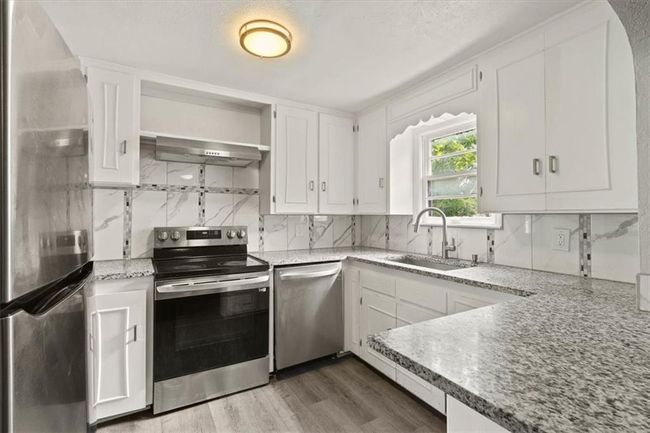Kitchen featuring appliances with stainless steel finishes, extractor fan, backsplash, white cabinets, and wood finished floors | Image 11