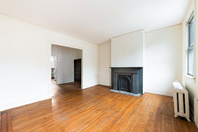 Unfurnished living room with a fireplace with flush hearth, baseboards, light wood finished floors, and radiator heating unit | Image 9