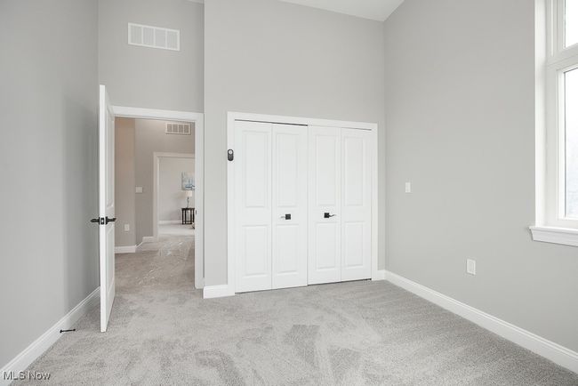 Unfurnished bedroom featuring light colored carpet, a high ceiling, a closet, and multiple windows | Image 23