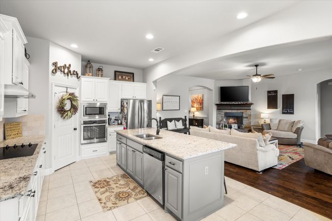 Kitchen with arched walkways, a center island with sink, stainless steel appliances, open floor plan, and white cabinets | Image 14