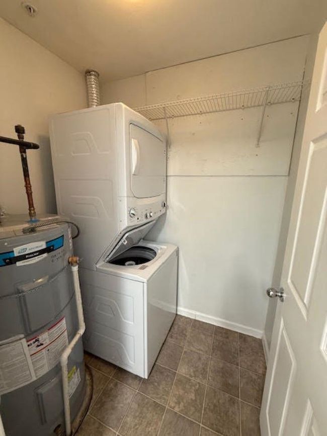 Clothes washing area featuring water heater, dark tile patterned floors, stacked washer and clothes dryer, and laundry area | Image 13