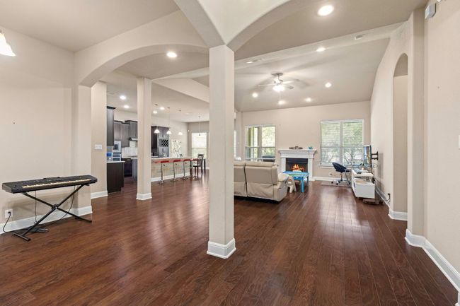 Living room featuring ceiling fan, a warm lit fireplace, dark wood finished floors, recessed lighting, and arched walkways | Image 6
