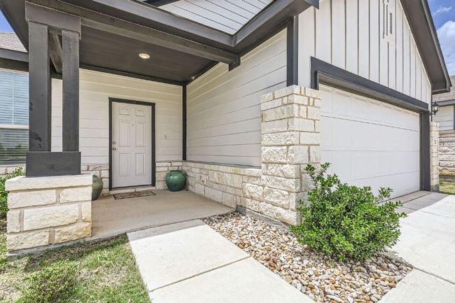 Doorway to property featuring board and batten siding, stone siding, a garage, covered porch, and driveway | Image 5