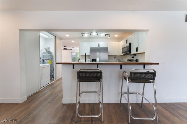 Kitchen with a kitchen breakfast bar, dark wood-style floors, washer / dryer, stainless steel appliances, and white cabinets | Image 13