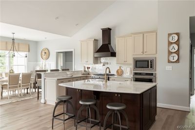 Kitchen featuring light hardwood / wood-style flooring, custom exhaust hood, cream cabinetry, a chandelier, and appliances with stainless steel finishes | Image 3