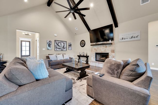 Living room with high vaulted ceiling, beamed ceiling, ceiling fan, a stone fireplace, and wood finished floors | Image 8