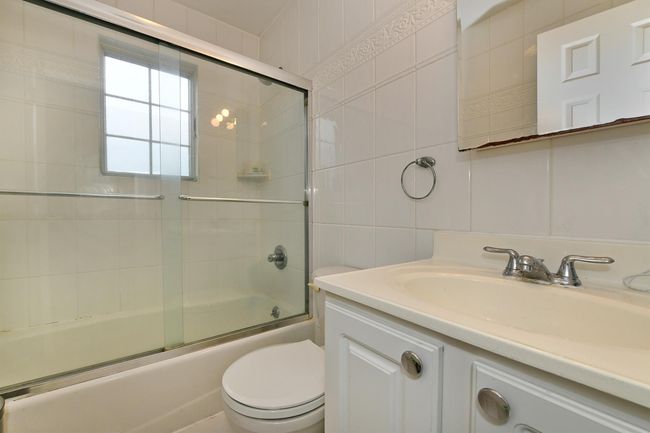 Full bath featuring enclosed tub / shower combo, toilet, vanity, and tile walls | Image 18