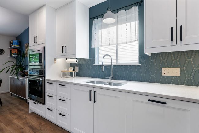 Kitchen with a sink, tasteful backsplash, dark wood finished floors, white cabinetry, and appliances with stainless steel finishes | Image 15
