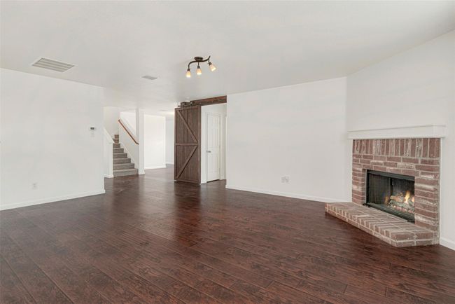 Unfurnished living room with dark wood-style flooring, a brick fireplace, baseboards, and stairs | Image 15
