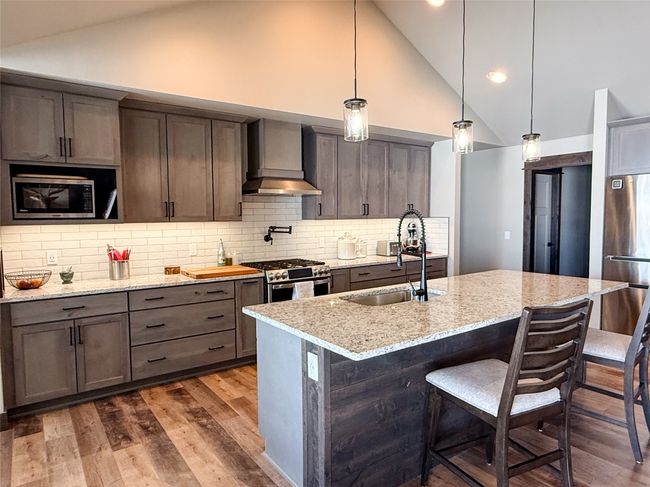 Kitchen with dark wood finished floors, stainless steel appliances, a sink, wall chimney range hood, and light stone countertops | Image 11