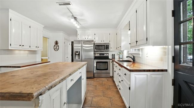 Kitchen with appliances with stainless steel finishes, white cabinetry, stone finish flooring, wood counters, and backsplash | Image 38