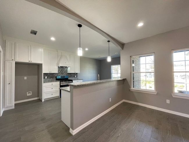 Looking in kitchen featuring stainless steel gas range, wood-style flooring, white cabinets, and tasteful backsplash | Image 6