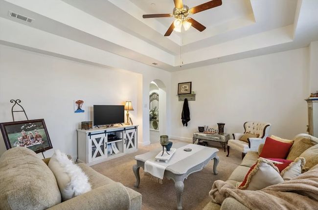 Living room featuring visible vents, a tray ceiling, arched walkways, light colored carpet, and ceiling fan | Image 24