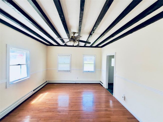 Unfurnished room featuring baseboard heating, beam ceiling, wood finished floors, and ceiling fan | Image 4