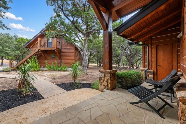 This view from the main patio reveals a charming guest house with its own private entrance and elevated deck. The stone pathway and rustic landscaping enhance the property’s natural aesthetic, while comfortable patio seating invites relaxation in the shade of surrounding trees. | Image 26