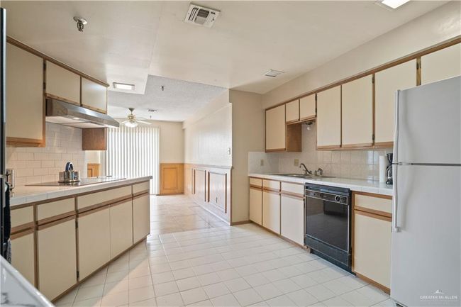Kitchen with black appliances, under cabinet range hood, tile counters, wainscoting, and ceiling fan | Image 6
