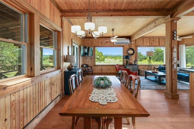 Dining area featuring wood walls, beam ceiling, light wood-style floors, and ceiling fan with notable chandelier | Image 12