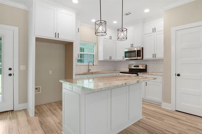 Bright, modern kitchen with white cabinetry, sleek stainless steel appliances, and a spacious marble island. Features stylish pendant lighting, subway tile backsplash, and wood-look flooring, creating a warm and inviting atmosphere. | Image 7
