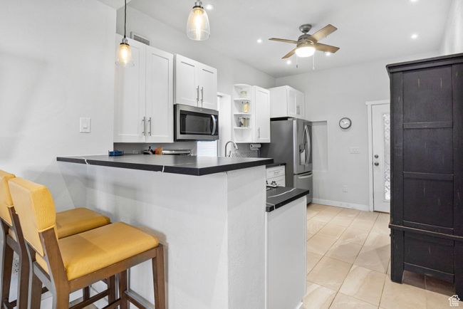 Kitchen with open shelves, dark countertops, appliances with stainless steel finishes, a kitchen breakfast bar, and a ceiling fan | Image 22