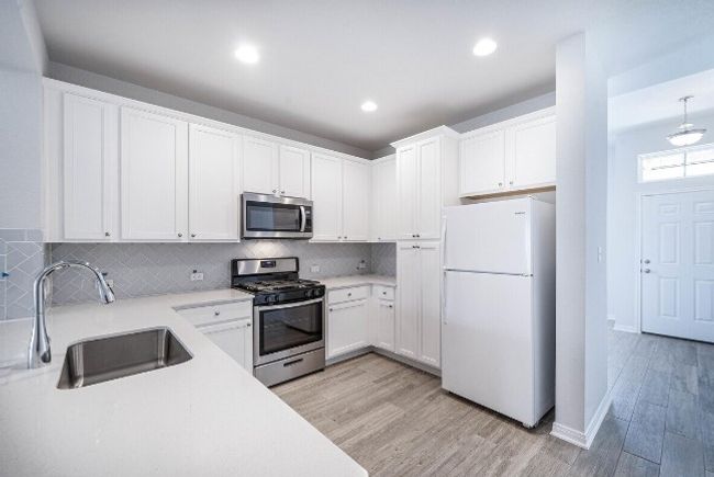 Kitchen featuring stainless steel appliances, light wood finished floors, tasteful backsplash, white cabinetry, and light countertops | Image 19