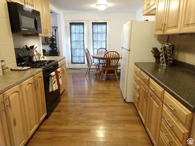Kitchen with french doors, tasteful backsplash, light wood-style flooring, dark countertops, and black appliances | Image 4