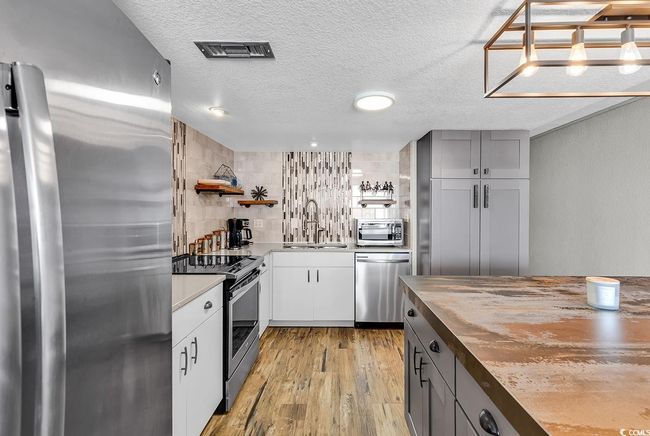 Kitchen featuring open shelves, light wood-type flooring, stainless steel appliances, a sink, and visible vents | Image 18