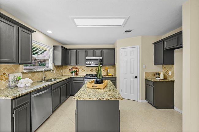 Kitchen with stainless steel appliances, a center island, light stone countertops, backsplash, and recessed lighting | Image 18
