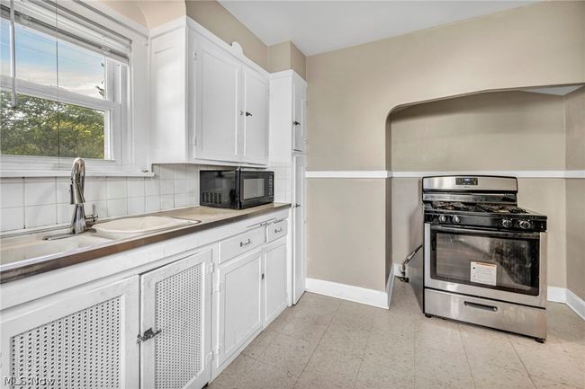 Kitchen with backsplash, white cabinets, stainless steel range with gas stovetop, and light tile floors | Image 9
