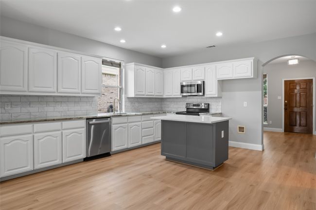Kitchen featuring stainless steel appliances, arched walkways, white cabinetry, tasteful backsplash, and recessed lighting | Image 5