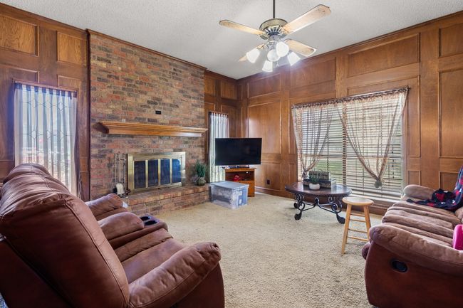 Living area with carpet, a brick fireplace, wood walls, and a wealth of natural light | Image 39