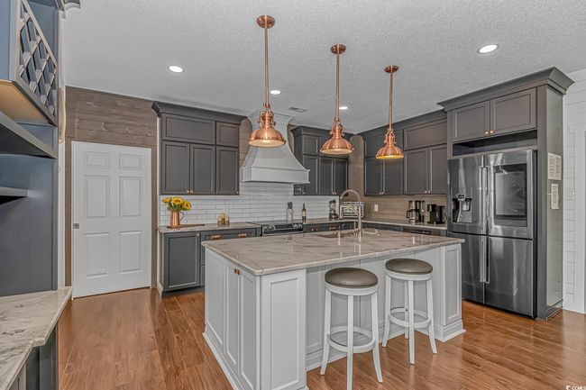 Kitchen with stainless steel refrigerator with ice dispenser, a sink, light stone counters, tasteful backsplash, and wood finished floors | Image 11
