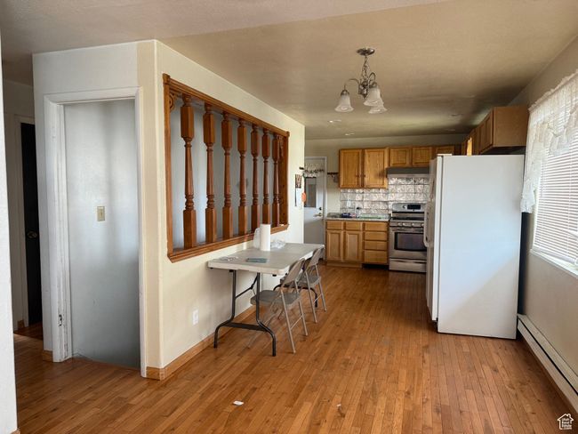Kitchen featuring light wood finished floors, an inviting chandelier, stainless steel range with gas stovetop, freestanding refrigerator, and a baseboard radiator | Image 9