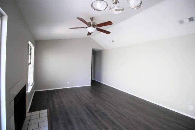 Unfurnished living room with vaulted ceiling, ceiling fan, dark wood-style floors, and a chandelier | Image 7