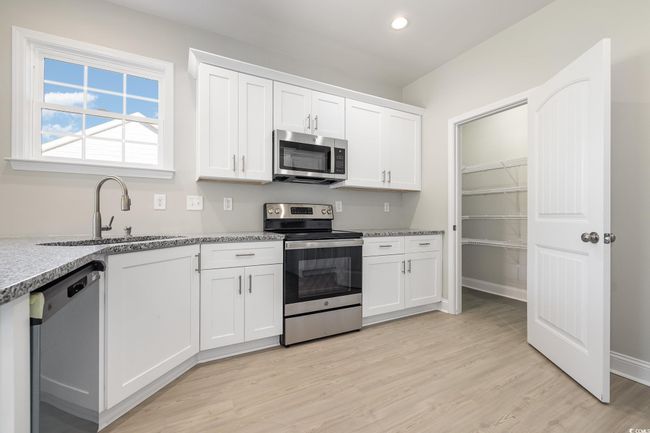 Kitchen featuring sink, light hardwood / wood-style flooring, light stone countertops, white cabinetry, and stainless steel appliances | Image 13