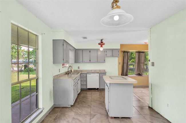 Bright and spacious kitchen with ample counter space, sleek gray cabinetry, and large windows offering a view of the lush backyard. Perfect for cooking enthusiasts and entertaining guests. | Image 14
