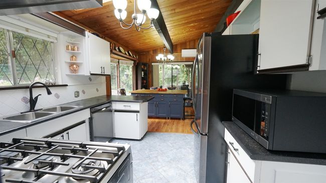 Kitchen featuring dark countertops, white cabinets, a notable chandelier, and a sink | Image 5