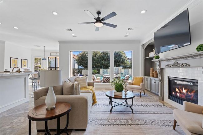 Another perspective of the living room, highlighting the pool view framed by large windows. The fireplace, built-ins, and easy access to the kitchen create an ideal space for entertaining and daily living. | Image 9