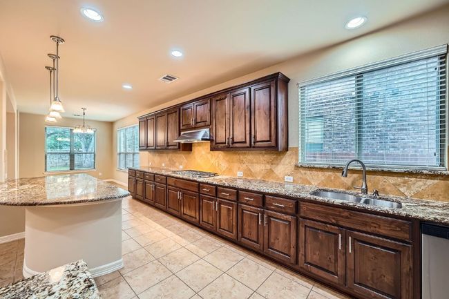 Kitchen featuring appliances with stainless steel finishes, under cabinet range hood, tasteful backsplash, light stone counters, and dark brown cabinets | Image 10