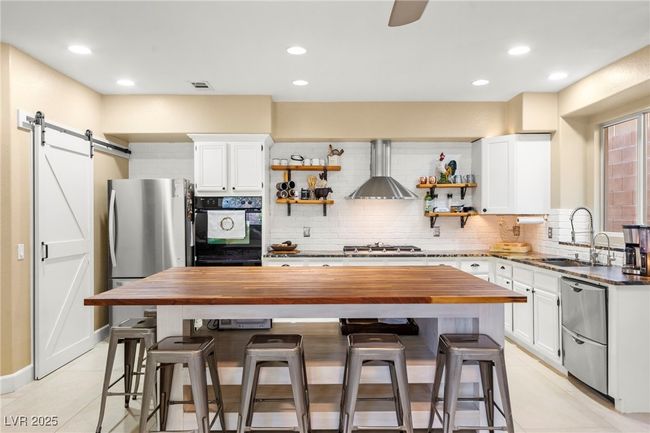 Kitchen with wall chimney range hood, a sink, stainless steel appliances, butcher block counters, and open shelves | Image 10