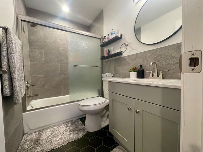 Full bathroom featuring vanity, tile walls, enclosed tub / shower combo, toilet, and tile patterned flooring | Image 17