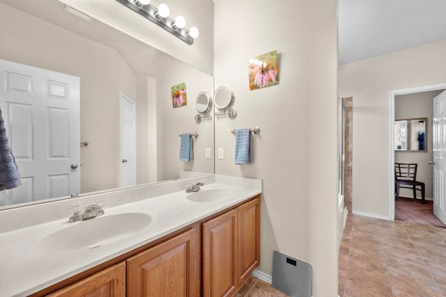 Dual vanities, bright lighting, and tile flooring make up the primary bathroom. | Image 13