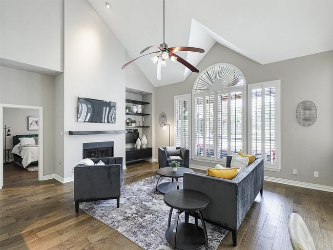 Living room with a ceiling fan, a glass covered fireplace, high vaulted ceiling, dark wood-style floors, and built in shelves | Image 20