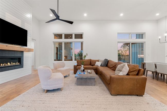 Living room with wood finished floors, recessed lighting, a large fireplace, ceiling fan, and a towering ceiling | Image 4