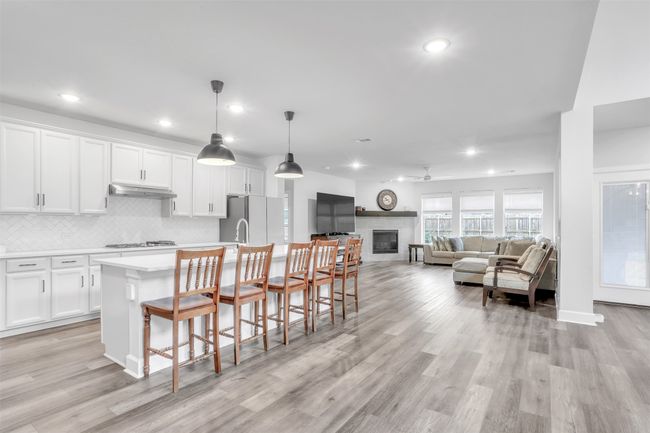 Kitchen featuring white cabinetry, white refrigerator, an island with sink, pendant lighting, and decorative backsplash | Image 10
