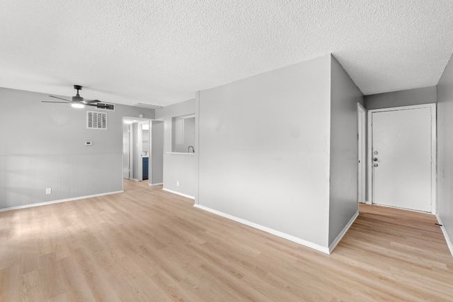 Unfurnished living room with a textured ceiling, light wood-type flooring, ceiling fan, baseboards, and visible vents | Image 5