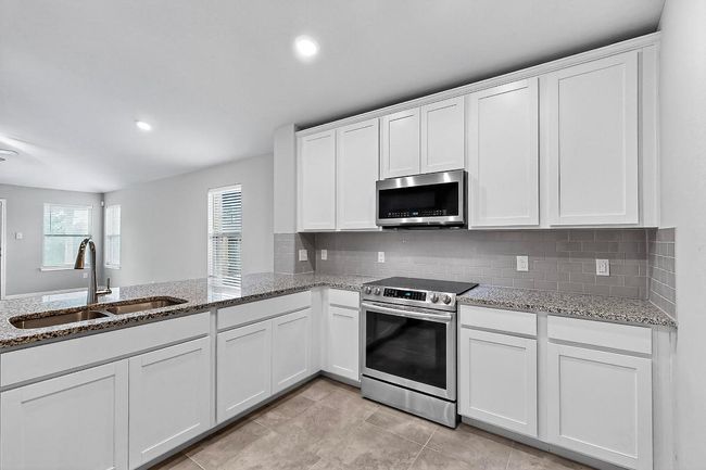 Kitchen with stainless steel appliances, white cabinets, decorative backsplash, light stone counters, and light tile patterned flooring | Image 12