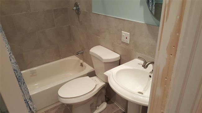 Full bathroom with toilet, shower / tub combo with curtain, tile walls, tile patterned floors, and sink | Image 7